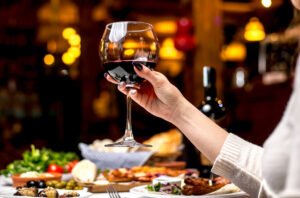 Kobieta trzyma lampkę wina na zastawionym stołem - Lampka wina codziennie - czy jestem alkoholikiem
