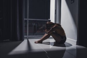 Młoda dziewczyna siedzi pod ścianą w ciemnym pokoju. Depresja u nastolatków — jak ją rozpoznać