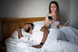 Kobieta przegląda telefon śpiącego partnera. Zazdrość w związku — czy to normalne, że ją czuję