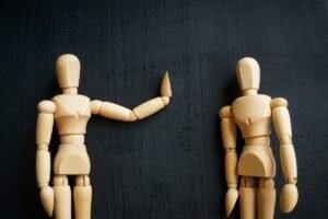 Dwie figurki na ciemnym tle, jedna niewerbalnie mówi nie - Znaczenie asertywności w zdrowiu psychicznym
