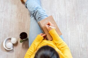 Kobieta siedzi na podłodze i wypisuje noworoczne postanowienia