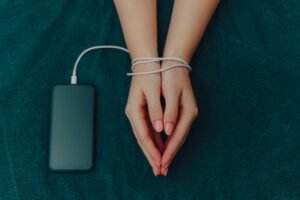 Uzależnienie behawioralne - kobiece ręce związane ładowarką do telefonu